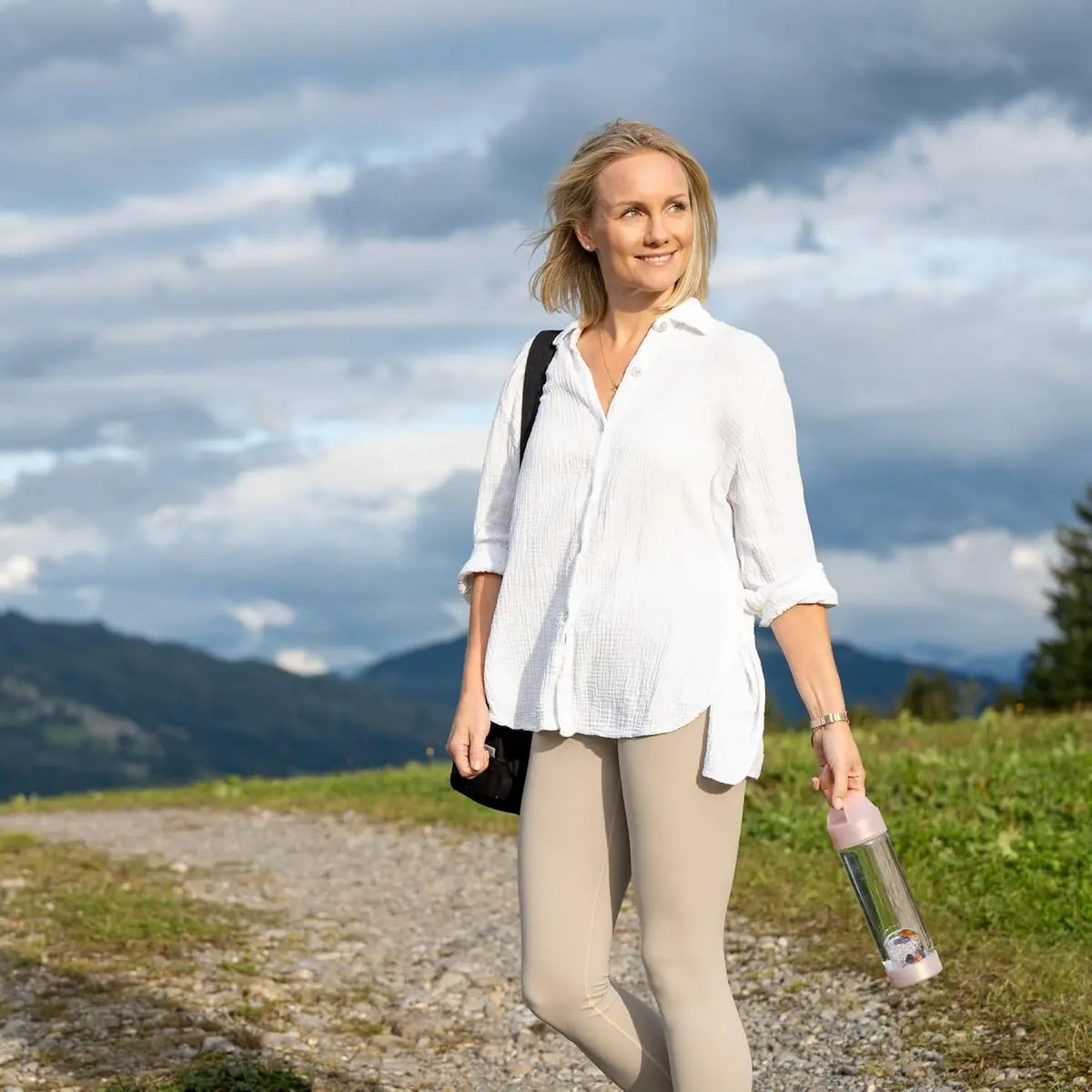 Femme souriante tenant la bouteille en verre VitaJuwel ViA Prana Rose avec pierres précieuses