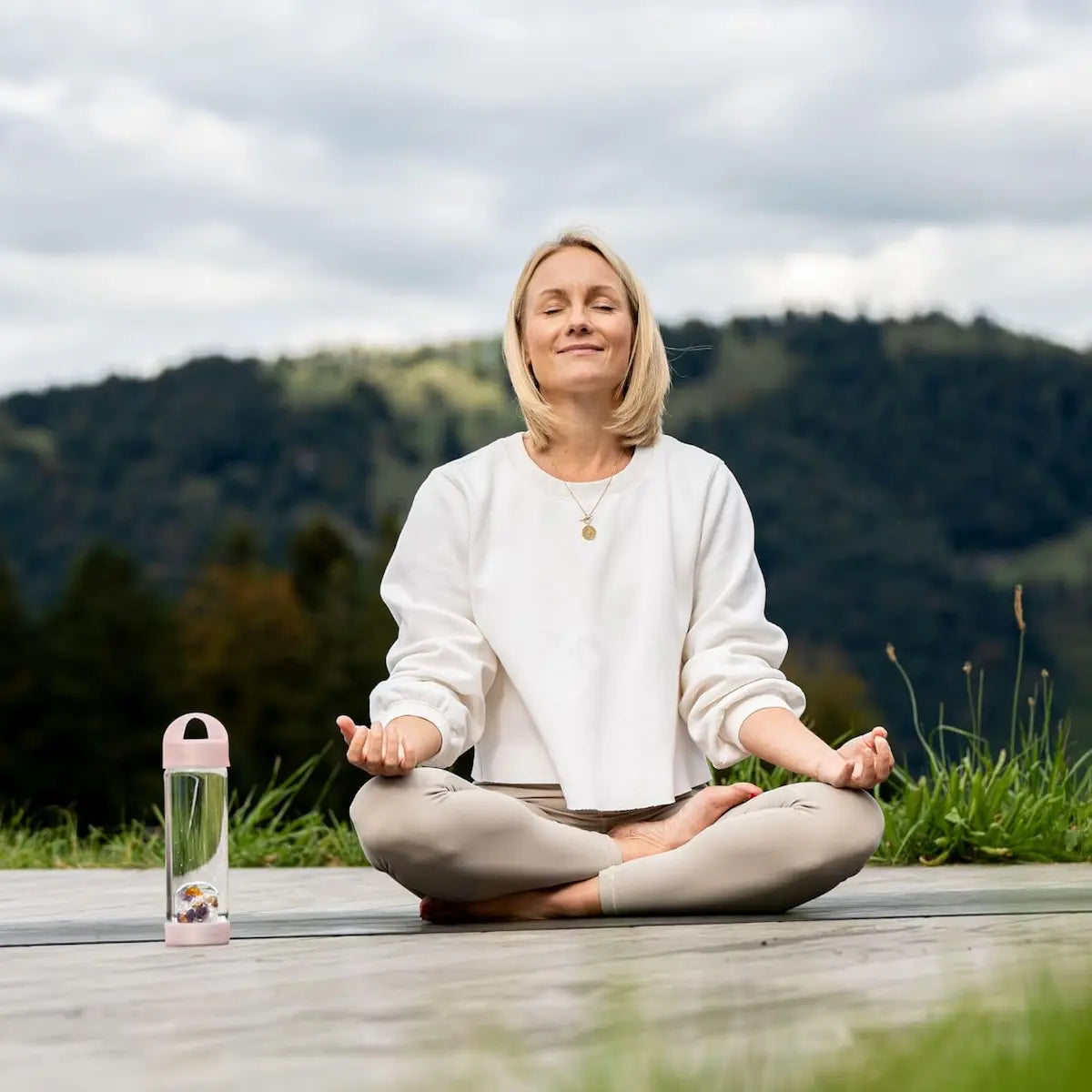 Moment bien-être : femme assise en tailleur avec la bouteille VitaJuwel Prana Rose