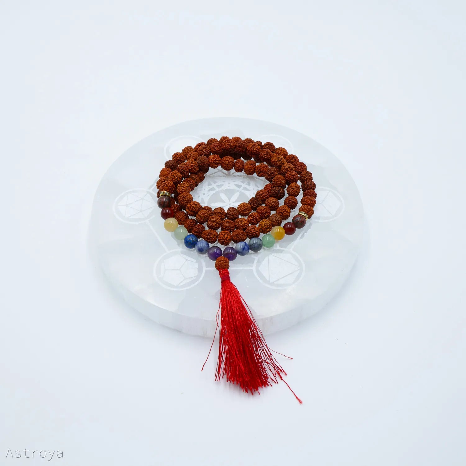 Mala Rudraksha 7 chakras sur une pierre de chargement en sélénite disponible également sur Astroya.fr