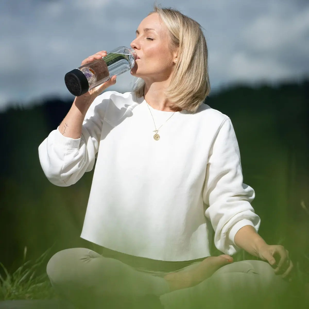 Moment bien-être : femme assise en tailleur tenant une bouteille d’eau vitalisée VitaJuwel Prana Noire