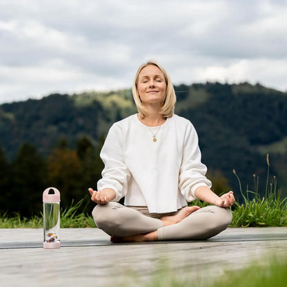 Moment bien-être : femme assise en tailleur avec la bouteille VitaJuwel Prana Rose 