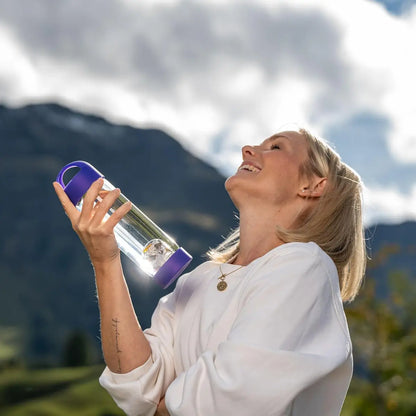 Femme souriante tenant la bouteille en verre borosilicate VitaJuwel ViA Prana Violet avec pierres précieuses